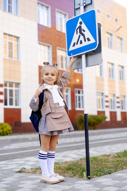 Фото Школьница переходит дорогу по пешеходному переходу, направляясь в школу или домой, или стоит у дорожного знака, указывая на него пальцем, изучая правила дорожного движения