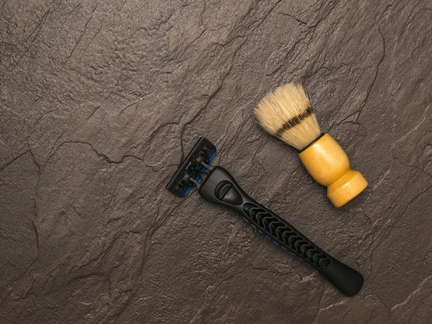 Фото Кисточка для бритья с деревянной ручкой и синей бритвой на каменном фоне. набор для ухода за мужским лицом. плоская планировка.
