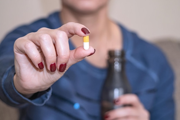 Фото Больная женщина держит в руке таблетку, принимает обезболивающие, концепция фармацевтического лечения людей крупным планом