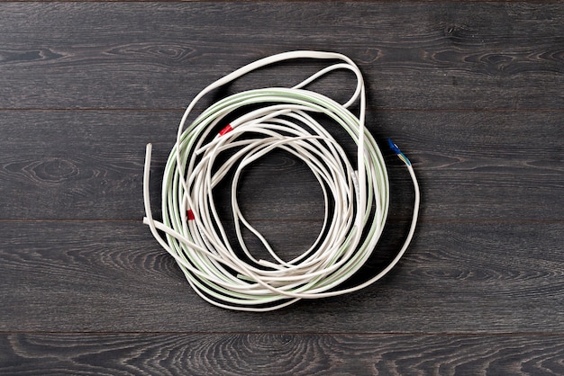 Фото Простой белый провод, плоский провод, лежащий на деревянной изолированной поверхности, промышленное подключение к сети