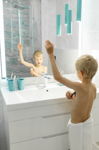 Фото Шестилетний мальчик бреет подмышки электробритвой в ванне перед зеркалом, гигиена по утрам