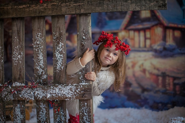 写真 自然な木製の柵の近くで彼女の頭にナナカマドの花輪を持つ小さな子供の女の子