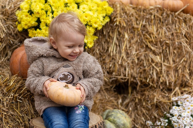 写真 小さな子供が干し草の背景にカボチャを手に持っている