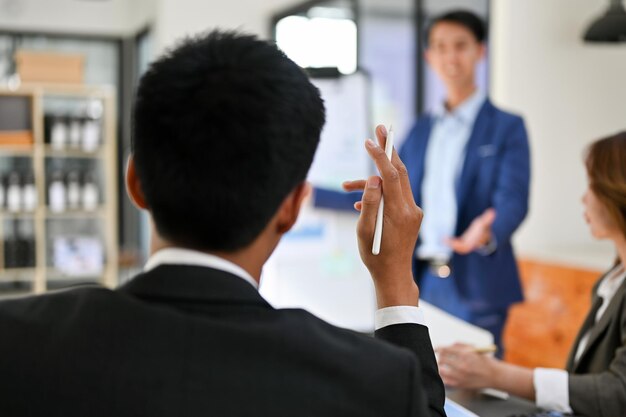 写真 スマートなアジア系のビジネスマンが挙手し、会議中に質問をする