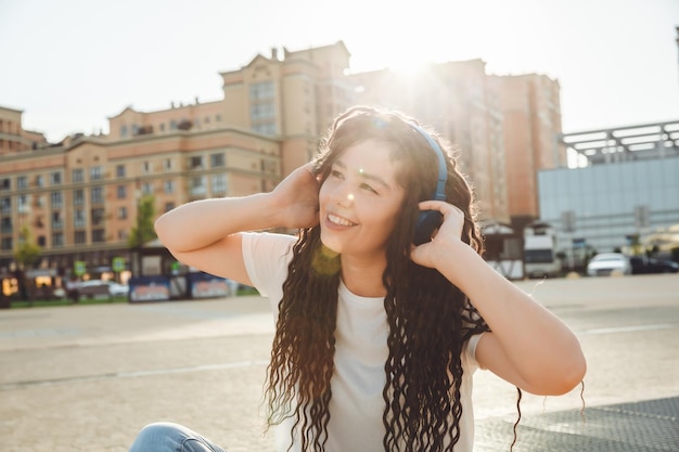 写真 ヘッドフォンでドレッドヘアを持つ笑顔の女の子が公園の床に座っています ヘッドフォンで音楽を楽しんでリラックスする幸せな若い女性 世代 z をコピーするためのスペース