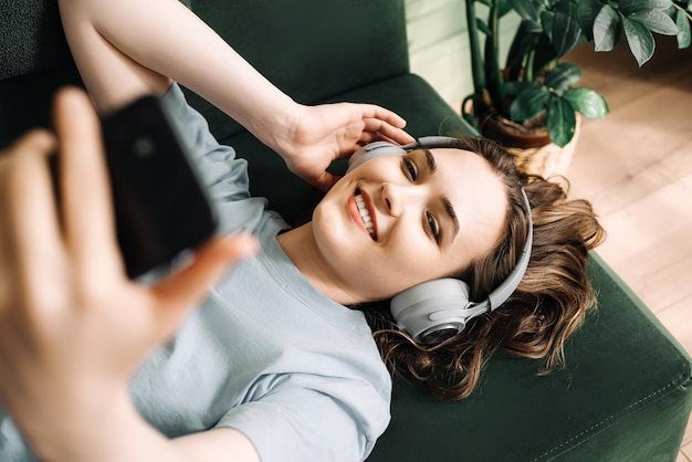 写真 ワイヤレスヘッドホンをかぶった笑顔の若い中年女性がコーンに横たわって音楽を聴いています