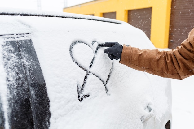 Заснеженная машина зимой стоит на улице. снег на окнах машин. нарисованное сердце в снегу на окне машины