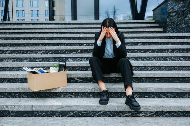 Фото Мрачная сцена женщины, сидящей на ступеньках и переживающей потерю работы и трудности с безработицей. недовольная брюнетка, сидящая на лестнице после потери работы