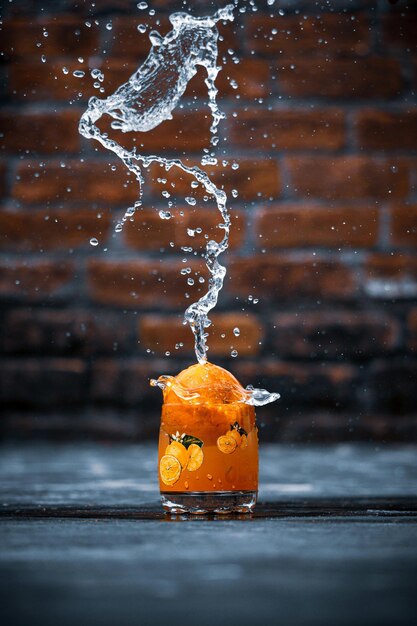 Фото Капля апельсинового сока с каплями воды, брызгающей на него
