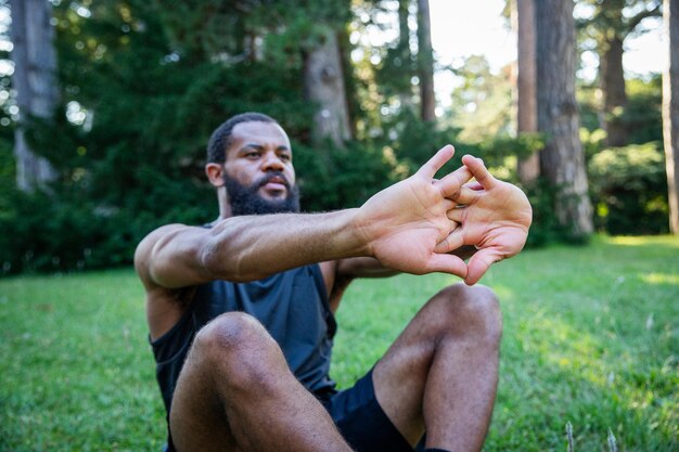 写真 スポーツ的なアフリカ人男性が草の上に座って腕を伸ばしている