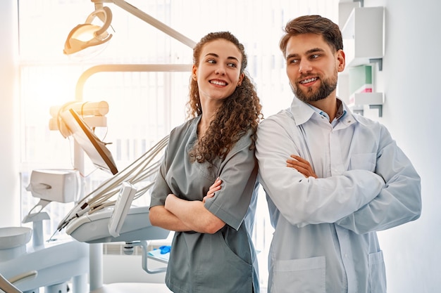 Фото Команда врачей в стоматологическом кабинете стоит спиной к спине, смотрит друг на друга и улыбается. работа и отдых врачей. копирование пространствасолнечный свет