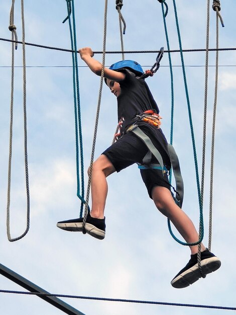 写真 ロープ遊園地の 10 代の白人の少年が吊り橋を渡る下からの眺め