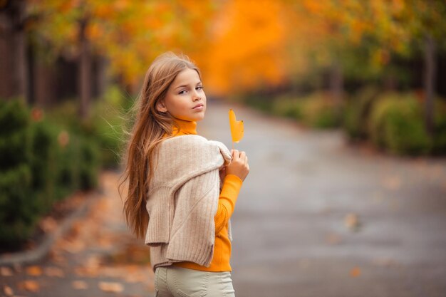 写真 黄色いスウェットを着た十代の女の子が ⁇ 秋に黄色い木の背景で街の外を歩いています