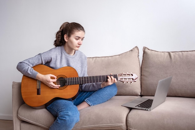 사진 소파에 있는 집에서 노트북 앞에서 기타를 치는 10대 여성