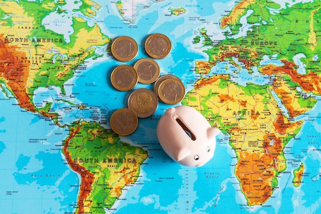 写真 小さな貯金箱がお金の旅行の概念の隣にある世界のカラフルな地図の上に立っています