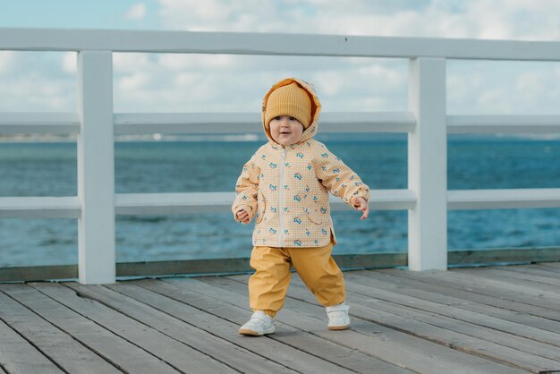 写真 黄色いジャケットとズボンを着た幼児が桟橋を歩いている