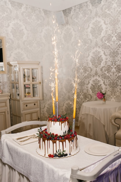 長年のラズベリーとブラックベリーと花火の噴水のある2段式の白いウェディングケーキ