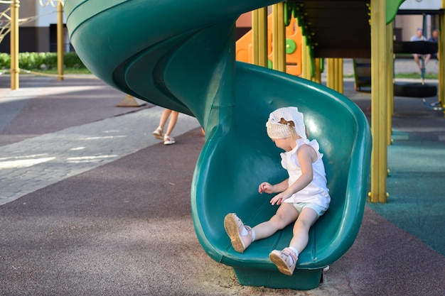 사진 2세 소녀가 어린이용 미끄럼틀에서 미끄러져 내려옵니다. 현대적인 놀이터 도시에서 활동적인 레크리에이션