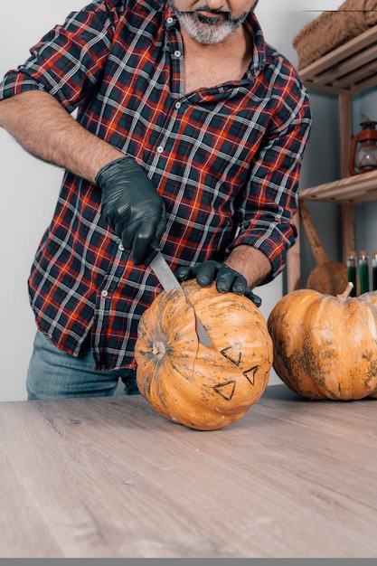 写真 ハロウィーンのためにカボチャを切っている間手袋をはめている人の垂直ショット