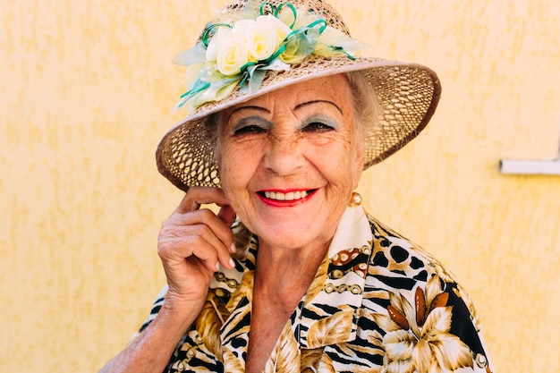 Очень старая женщина в шляпе с ярким макияжем возле своего дома