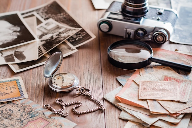 写真 チェーンの時計、古びた瓦礫の請求書、フィルムカメラ、木製のテーブルの白黒写真。ヴィンテージコレクションと過去への郷愁