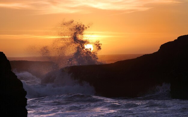 写真 a wave crashing into a cliff with the sun setting behind it