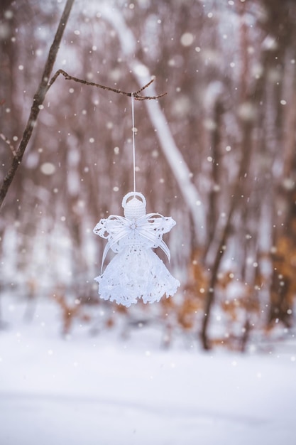 사진 마크라메로 만든 하얀 천사가 크리스마스의 상징인 눈 덮인 숲의 나뭇가지에 매달려 있다