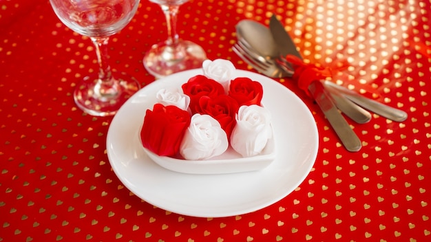 真っ赤にナイフとフォークが付いた白いプレート。赤と白のバラの装飾。バレンタインデーのテーブルセッティング