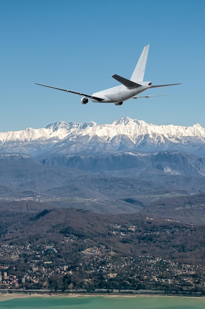 写真 白いワイドボディの飛行機が海辺のリゾートの山の町に飛んでいます