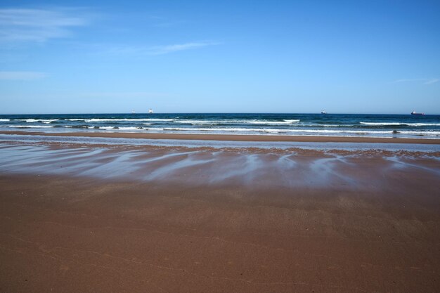 写真 浅い滑らかな砂の広いビーチ 遠くにはいくつかの船が海で航海しています