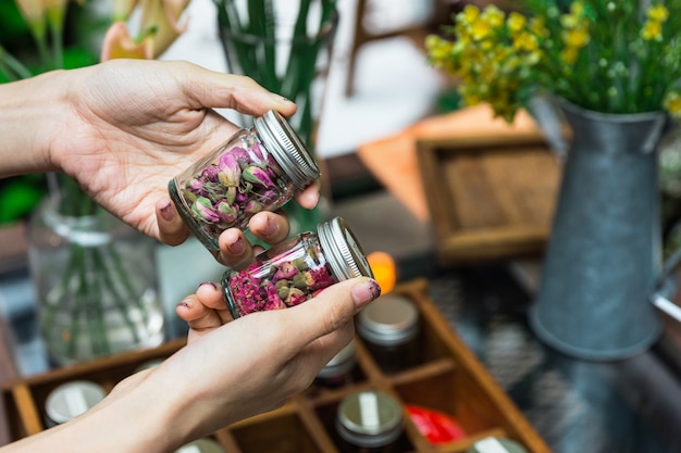 手にアルミ製の蓋が付いたガラス瓶で開花茶を作るためにドライフラワーを選ぶ女性。