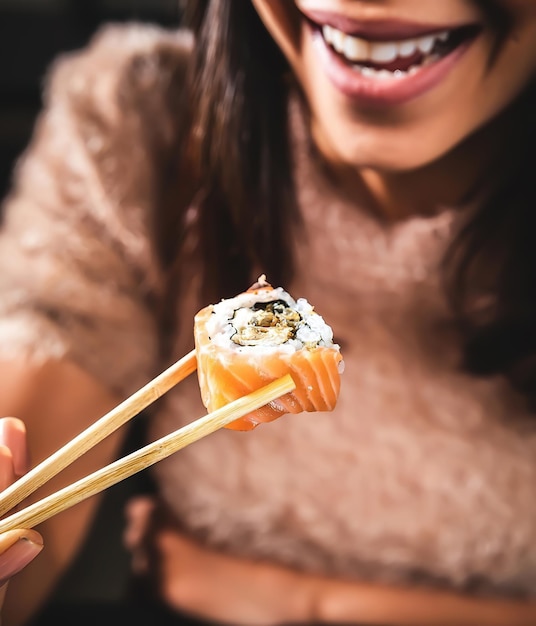 写真 お箸を使って笑顔で寿司を食べる女性。