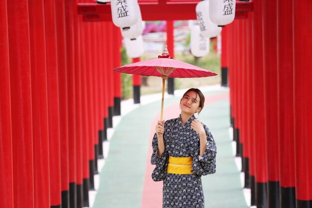 日本庭園の神社に傘をさして歩いている着物姿の女性。