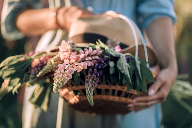 Фото Женщина держит корзину с полевыми цветами летние фиолетовые цветы в соломенной корзине люпиновое поле
