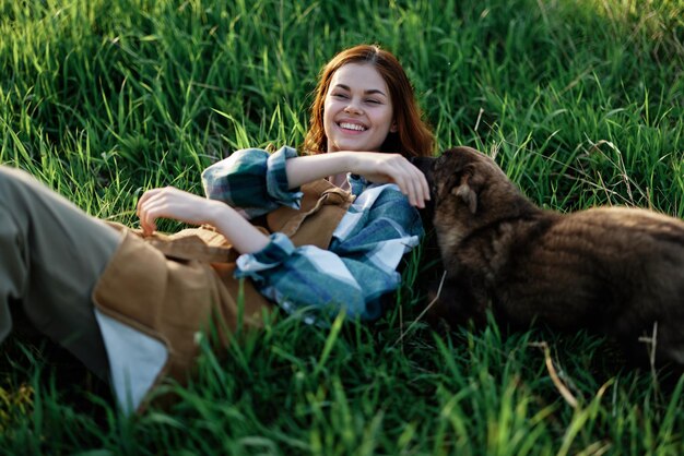 写真 草の上に横たわっている女性が夏の夕暮れの公園の自然の中で笑顔で犬を抱きしめています健康と動物への愛の概念カタツムリに対する治療高品質の写真