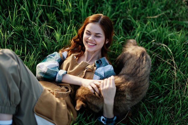 写真 夏の夕暮れの公園の自然の中で、笑顔で犬を抱きしめる女性が草の上に横たわっている。ダニに対する動物の治療と健康と愛のコンセプト