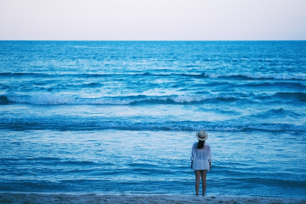 写真 ビーチに立って、美しい海と青い空を一人で見ている女性