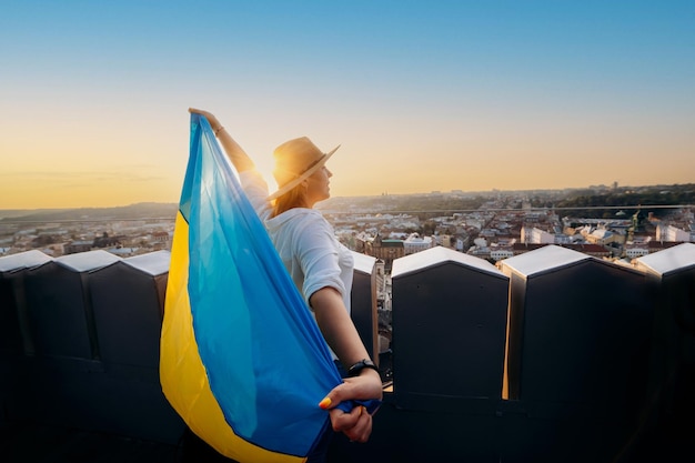 Фото Женщина стоит с национальным украинским флагом и размахивает им, молясь за мир на закате во львове. аа символ независимости и силы украинского народа молитесь за украину
