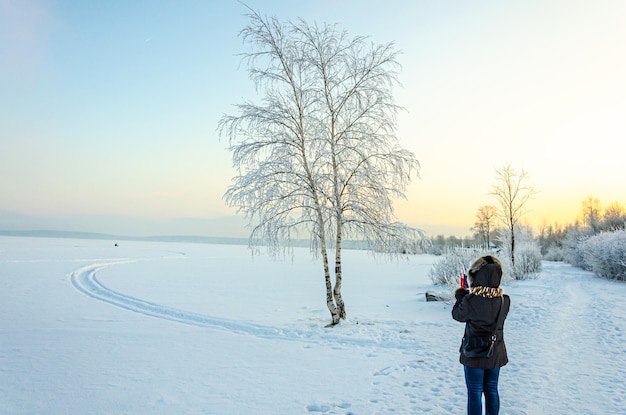 写真 雪景色の中、木の写真を撮る女性。