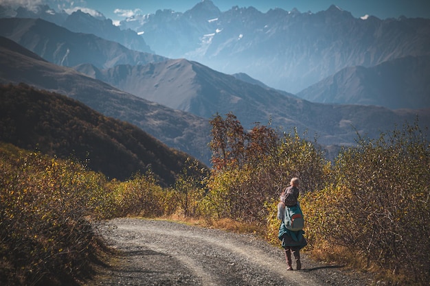 写真 山を背景に未舗装の道路を歩く女性。