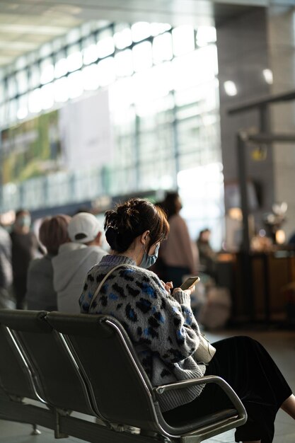 写真 フェイスマスクを着用した女性が空港の待合室に座っています。