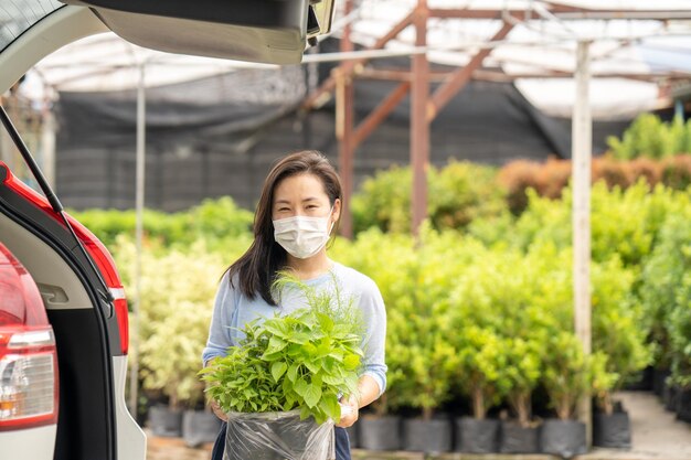 写真 マスクをした女性が手に植物の束を持って車の前に立っています。