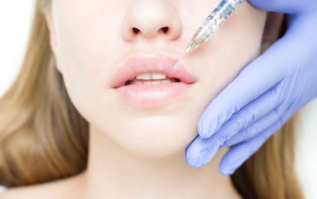 Фото Женщина с красивой чистой кожей косметолог делает инъекции для увеличения губ и против морщин красивой женщины женская косметология в салоне красоты увеличение губ