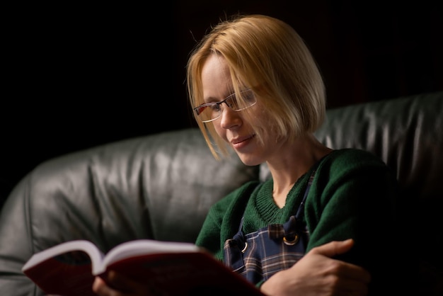 Фото Женщина в очках читает книгу дома на диване сорокалетняя женщина читает увлекательную книгу