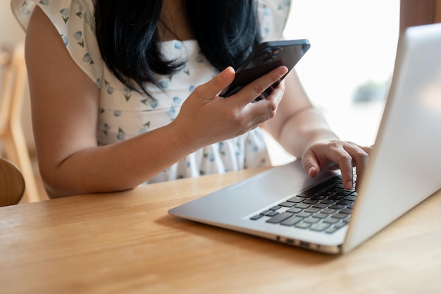 写真 スマートフォンを使ってラップトップのキーボードでタイピングするカフェでリモートで働く女性