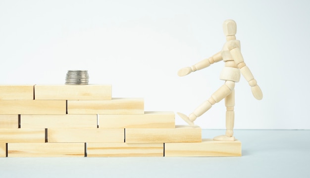 Фото Деревянный человек поднимается по ступенькам, чтобы добраться до стопки монет на белом фоне