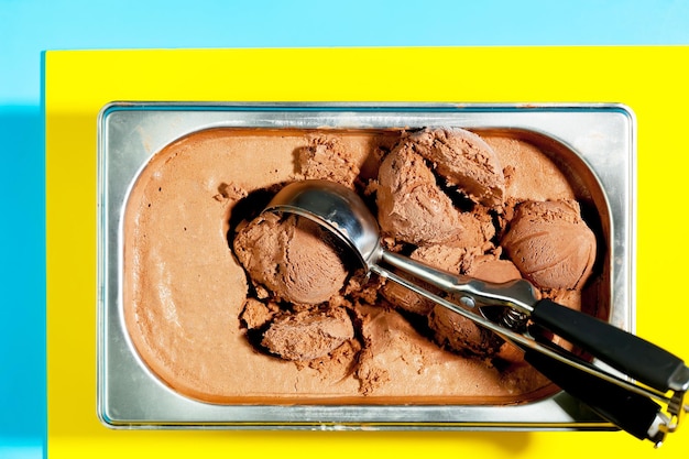 Фото Желтый контейнер шоколадного мороженого с ложкой в нем.