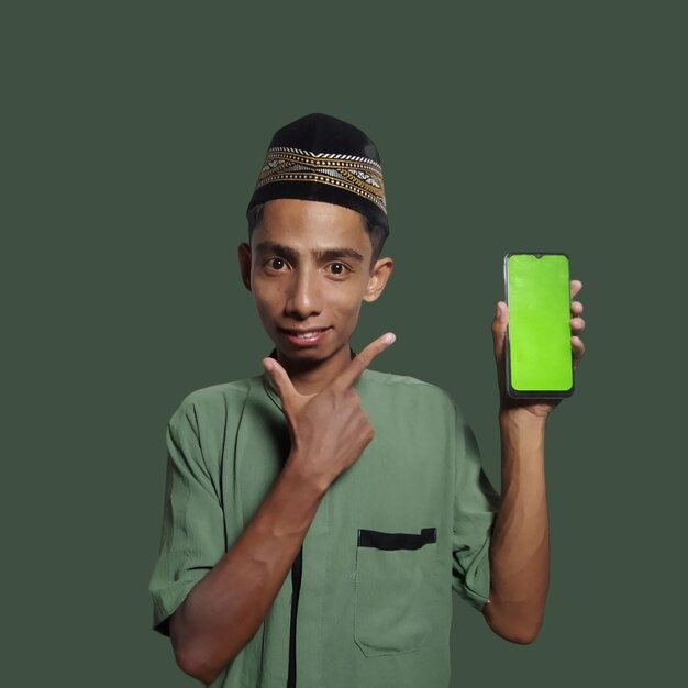Фото Молодой азиатский мусульманин в шапке, показывая экран мобильного телефона на зеленом фоне