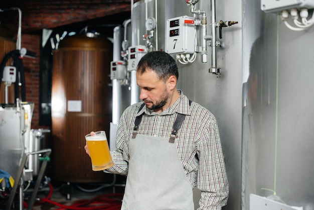 Фото Молодой бородатый пивовар проводит контроль качества свежесваренного пива на пивоварне.