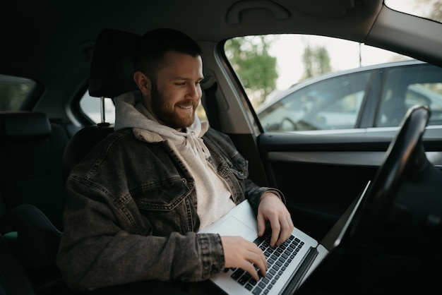 Фото Молодой бородатый мужчина с ноутбуком в автомобиле комфорта